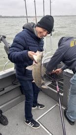 A young angler joyfully holding a Walleye while fishing on a boat, showcasing a successful catch during a chilly day on the water.