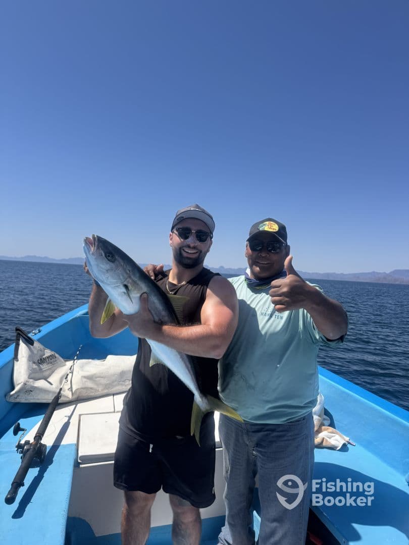 Two anglers proudly displaying a large Yellowtail while fishing on a boat in clear blue waters.
