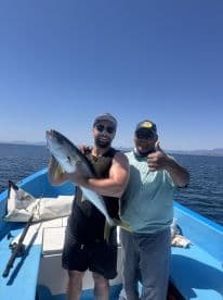 Two anglers proudly displaying a large Yellowtail while fishing on a boat in clear blue waters.