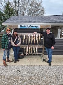 A group of three anglers proudly displaying their catch of Walleye on a board at Kott's Camp, showcasing a successful fishing trip.