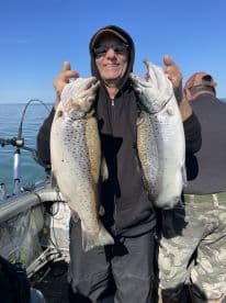 An angler proudly displaying two large Brown Trout while fishing on a calm lake, showcasing a successful day on the water.