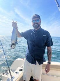 Angler proudly displaying a large fish while on a boat in open water, showcasing a successful fishing trip.