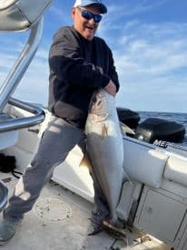 An angler joyfully displaying a large Amberjack aboard a fishing boat, showcasing a successful day on the water.
