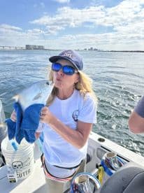 An angler joyfully poses with a Silver Pompano on a fishing boat, showcasing a successful catch during a sunny day on the water.
