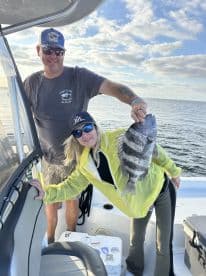 Two anglers proudly displaying a large Black Sea Bass aboard a fishing boat during a sunny day on the water.
