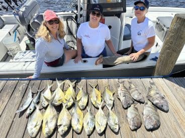 A group of three women proudly displaying their catch of Yellowtail Snapper and other species on a dock after a successful fishing trip.