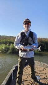 Young angler proudly holding a Speckled Trout while fishing from a boat in a grassy marsh environment.