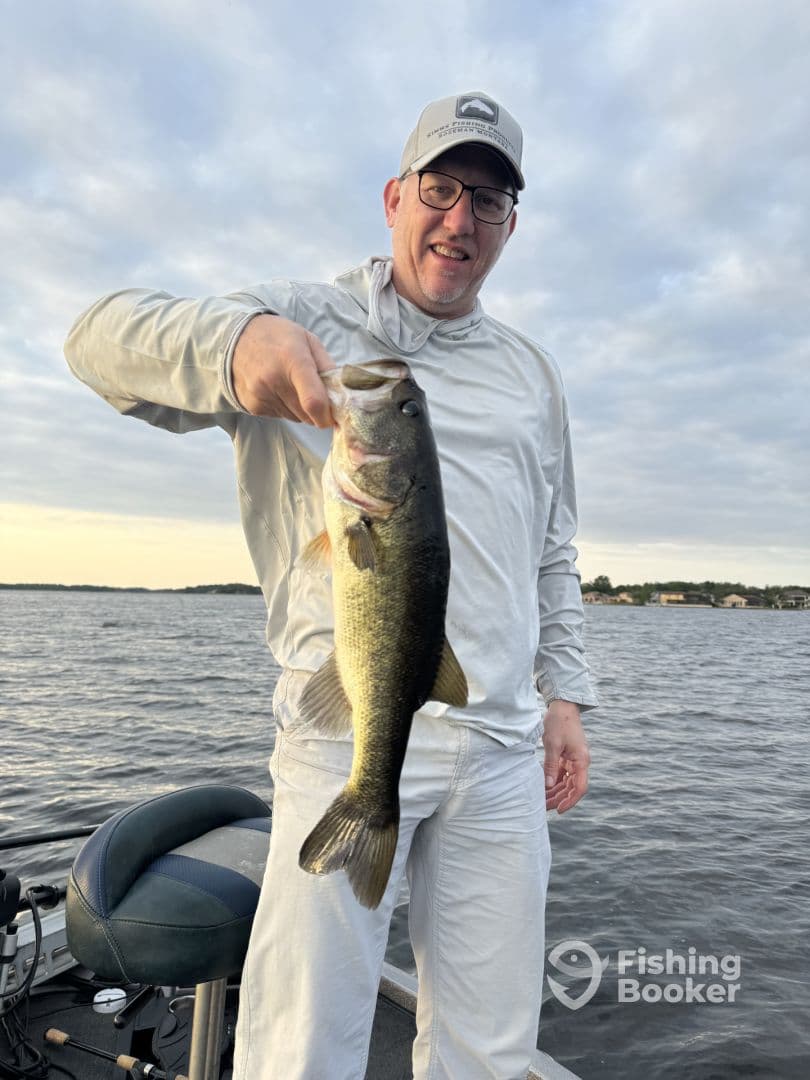 An angler proudly displaying a large Largemouth Bass while fishing on a serene lake during sunset.
