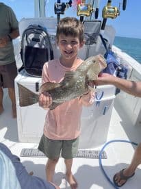 A young angler proudly displaying a large Grouper while fishing on a boat, showcasing a fun family fishing experience.