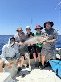 Group of anglers proudly displaying a large Grouper caught during a deep-sea fishing trip.