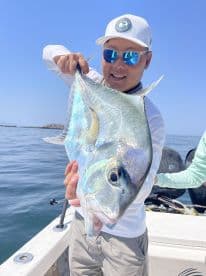Angler proudly displaying a vibrant fish while aboard a boat, showcasing a successful day of fishing in clear waters.