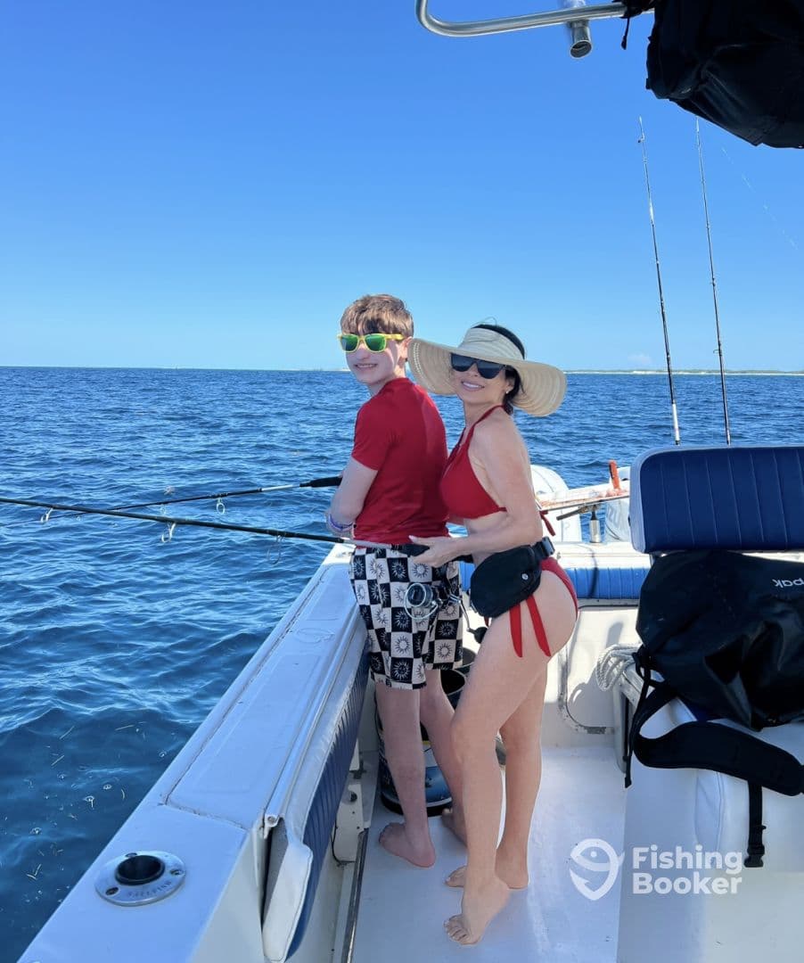 A mother and her son enjoying a fishing trip on a sunny day, both engaged with their fishing rods while on a boat in open water.