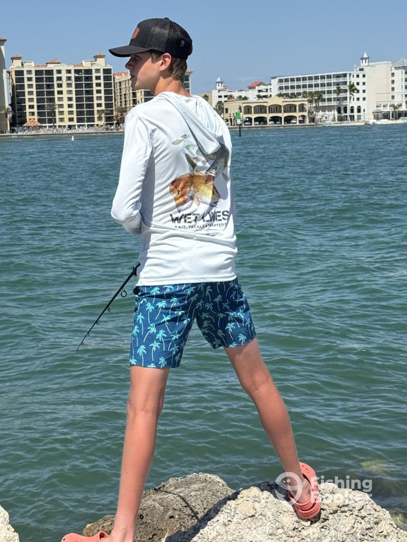 A young angler casting from a rocky shoreline, showcasing a vibrant fishing environment with buildings in the background.