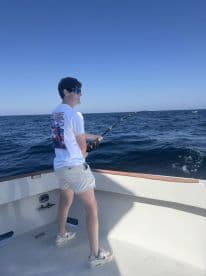 A young angler reeling in a catch while fishing on a boat in open waters, showcasing a sunny day at sea.