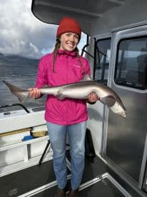 A young woman proudly displaying a caught shark aboard a fishing boat, showcasing the excitement of a successful fishing trip.