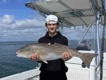 A young angler proudly displaying a large Redfish while aboard a fishing boat, showcasing a successful day on the water.