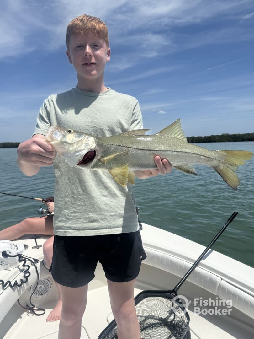 Young angler proudly holding a Snook while fishing on a sunny day in a coastal waterway.