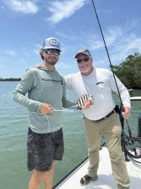 Two anglers proudly displaying a striped fish on a boat in a coastal fishing environment.