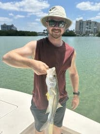 An angler proudly displaying a Snook caught while fishing in a scenic coastal area.