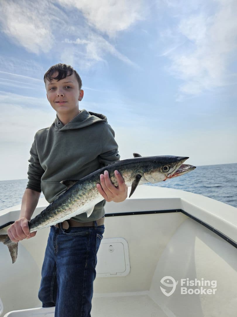 A young angler proudly holding a large King Mackerel while fishing offshore, showcasing a successful catch against a scenic ocean backdrop.