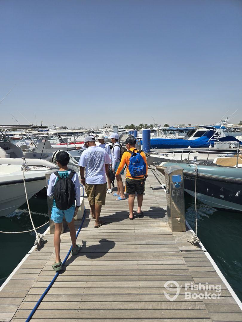 Group of anglers walking along the dock towards their fishing boat, showcasing a sunny day at the marina.