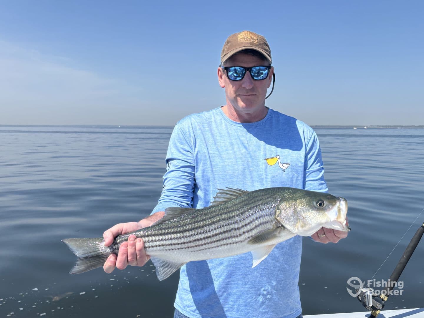 An angler proudly displaying a large Striped Bass while fishing on a calm day.