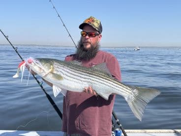 An angler proudly displaying a large Striped Bass while fishing on a clear day, showcasing the excitement of a successful catch.