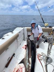 An angler proudly displaying a large Mahi Mahi aboard a sport fishing boat in open waters, showcasing a successful deep-sea fishing trip.