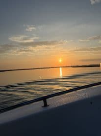 A serene sunset view from the side of a boat, reflecting on calm waters, showcasing a tranquil fishing environment.