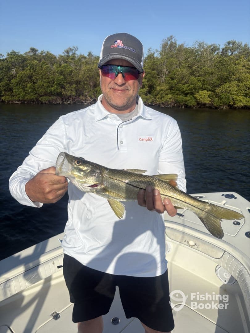 Angler proudly displaying a Snook caught while fishing from a boat in a mangrove area.