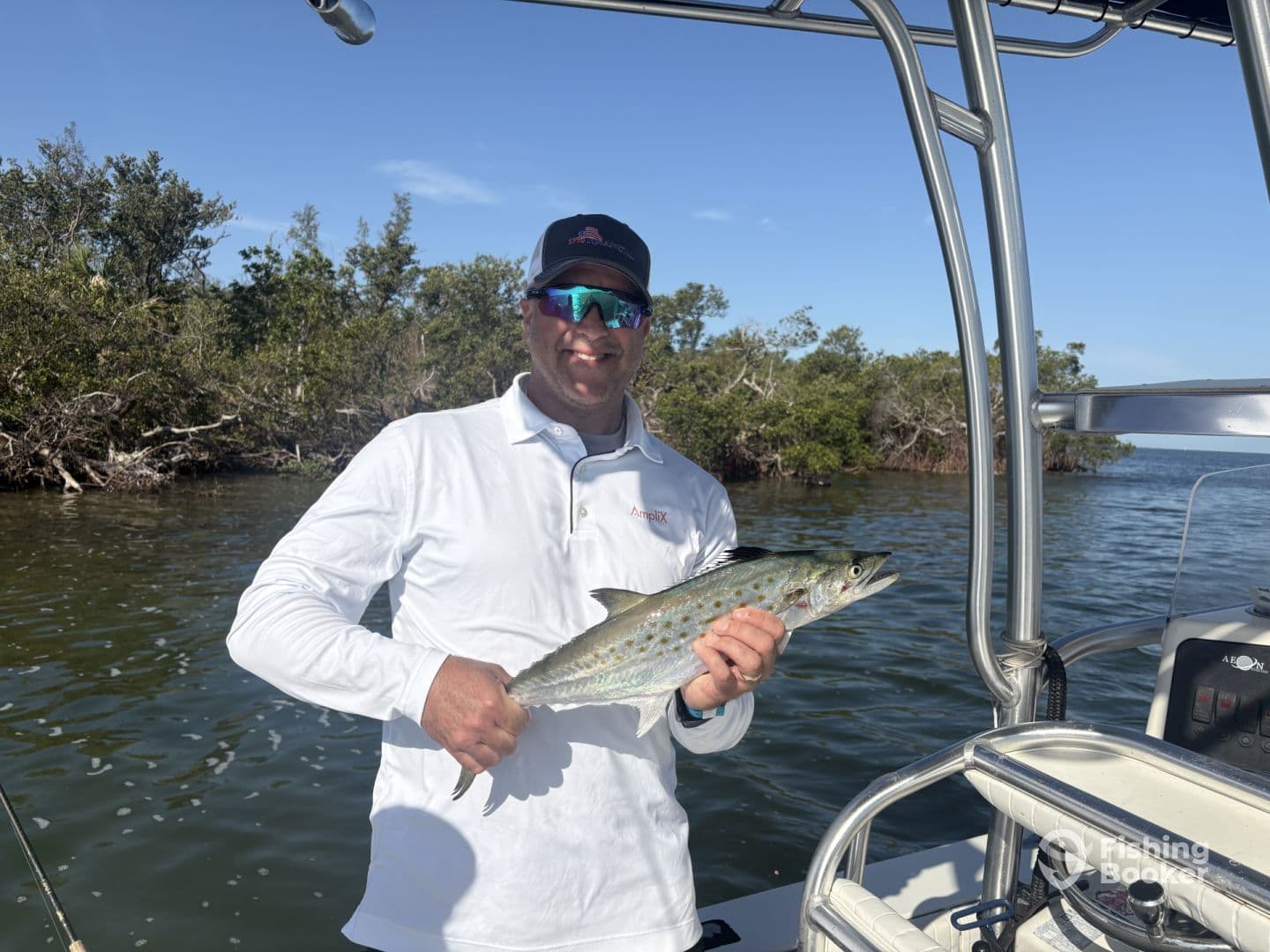 Angler displaying a beautiful Spanish Mackerel while fishing in a mangrove-lined area, showcasing a successful day on the water.