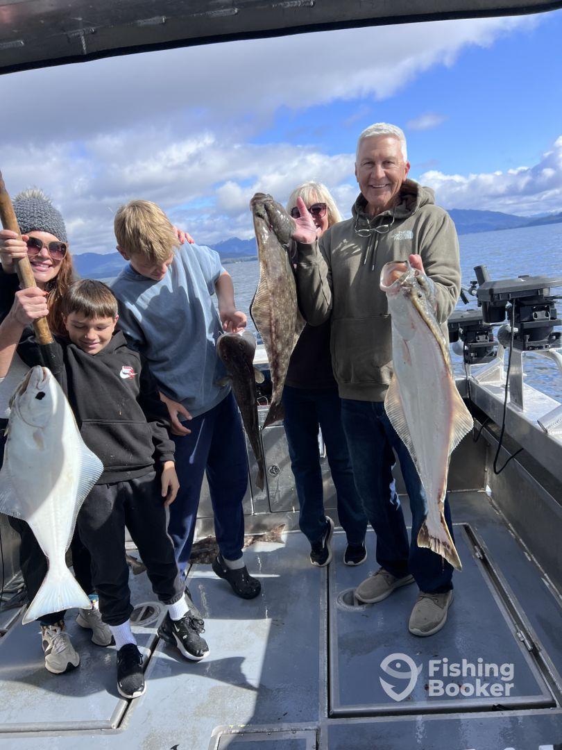A family proudly displaying their catch of halibut and other fish aboard a fishing boat, enjoying a day on the water.