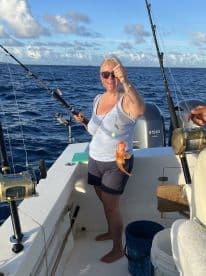 An angler proudly displaying a freshly caught fish while fishing on a boat in open water.