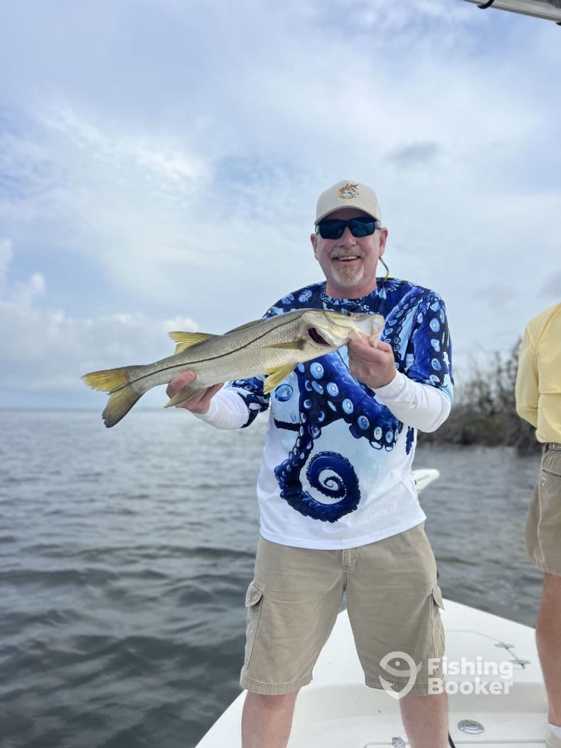 An angler proudly displaying a Snook while fishing from a boat in a coastal waterway.
