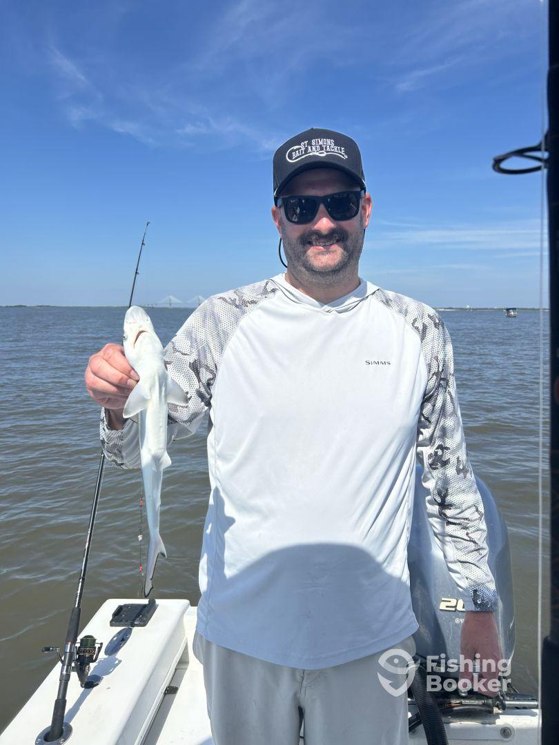 An angler proudly displaying a small fish while fishing on a boat in a coastal waterway.