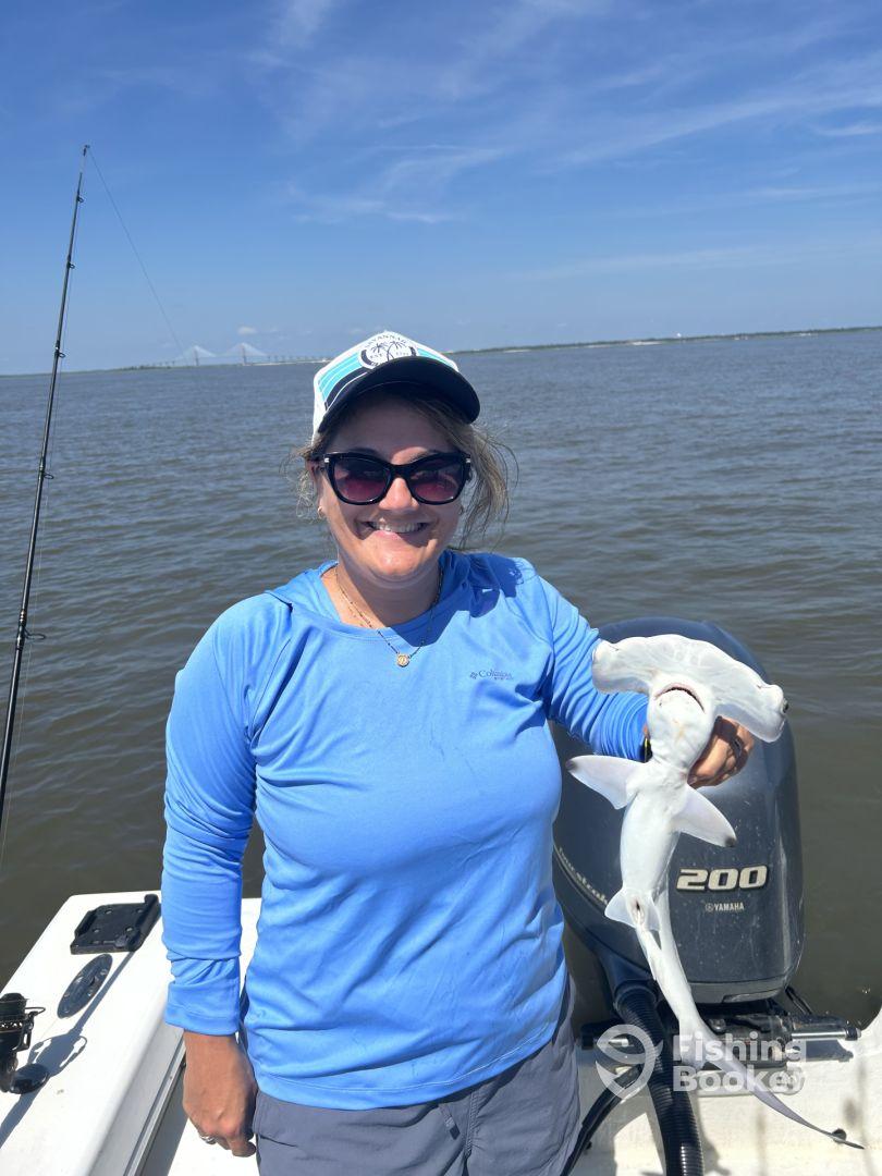 An angler proudly displaying a Hammerhead Shark while fishing on a boat in a coastal waterway.