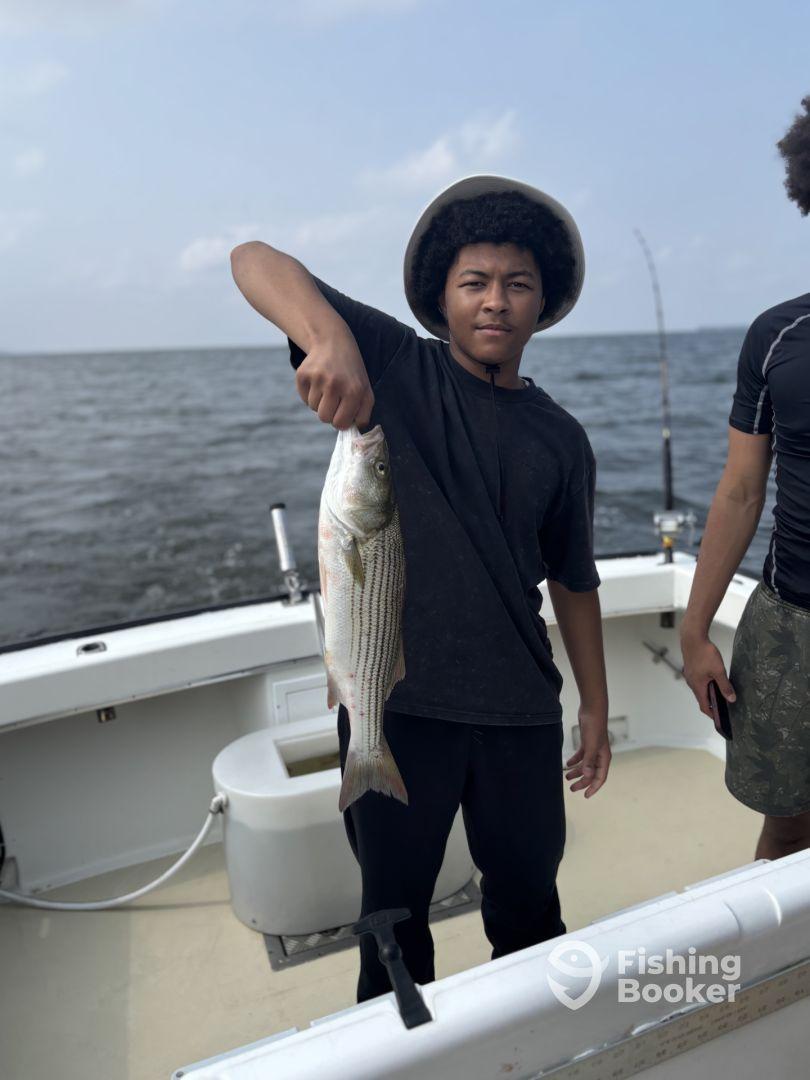 Young angler proudly displaying a striped bass while fishing on a boat, enjoying a day on the water.