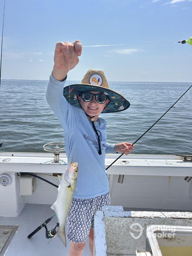 A young angler proudly displaying a caught fish while fishing on a boat in calm waters, showcasing a sunny day and a fun fishing experience.