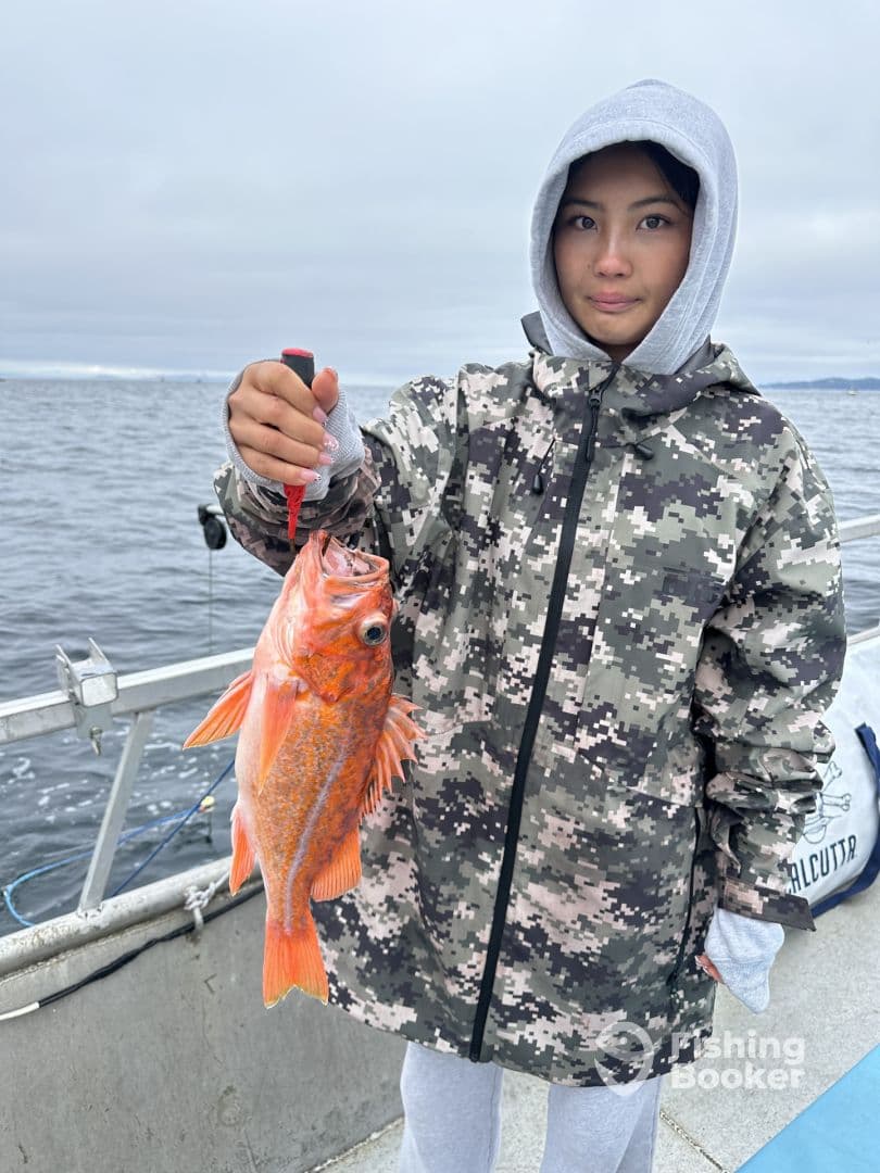 A young angler proudly displaying a vibrant Red Rockfish while fishing on a boat in a coastal environment.