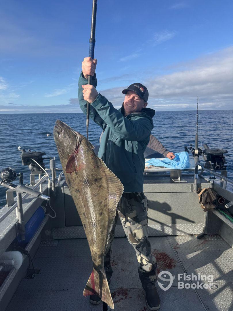 An angler proudly displaying a large Halibut while fishing on a boat in open waters.