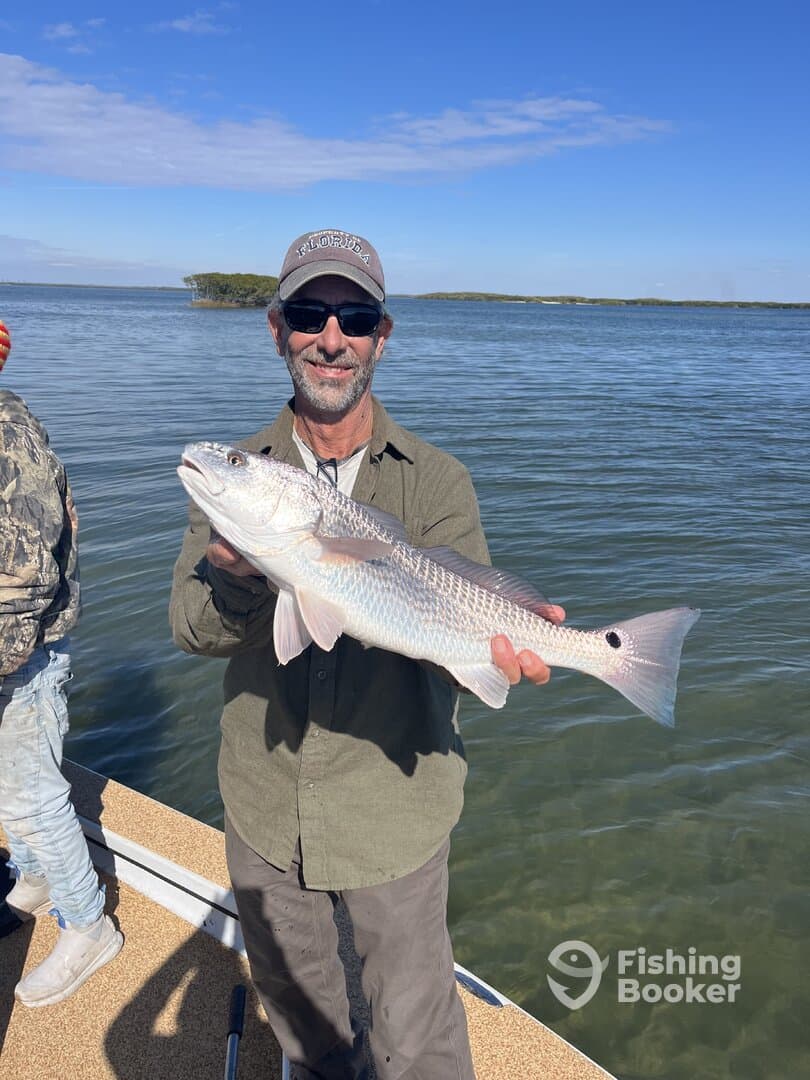 Angler proudly displaying a large Redfish while fishing in a scenic coastal environment.