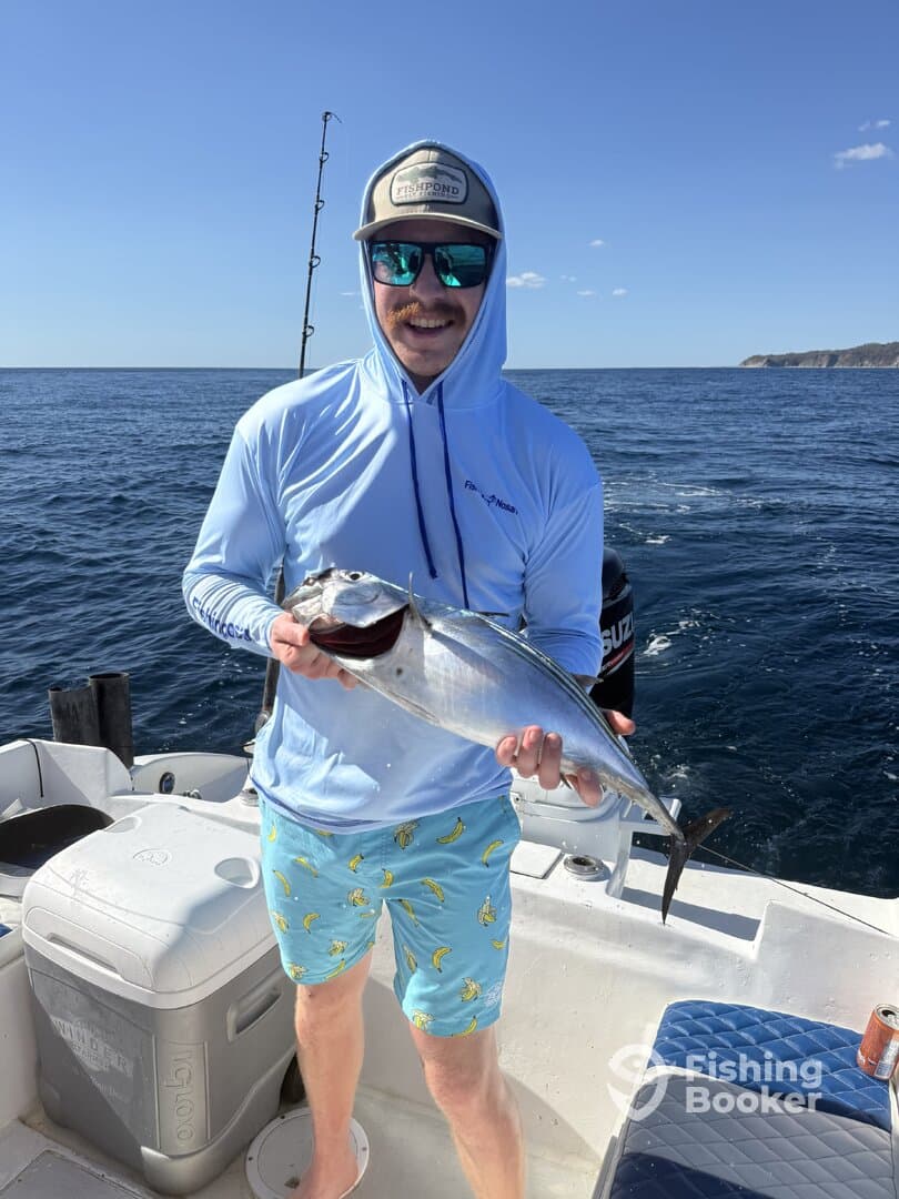 Angler proudly displaying a large fish while fishing on a sunny day, showcasing a vibrant ocean backdrop.