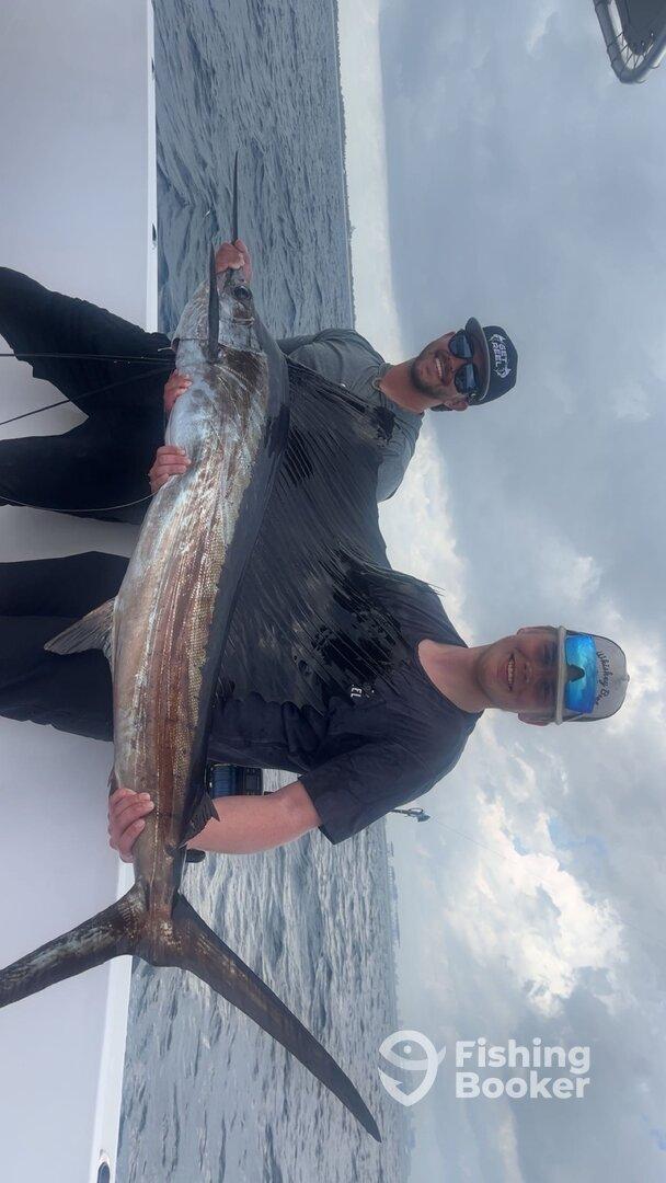 Two anglers proudly displaying a large Swordfish while fishing offshore, showcasing their successful catch.
