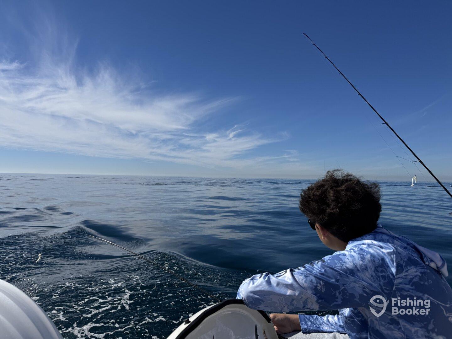 A young angler casting a line into the calm ocean waters, enjoying a serene day of fishing under a clear blue sky.