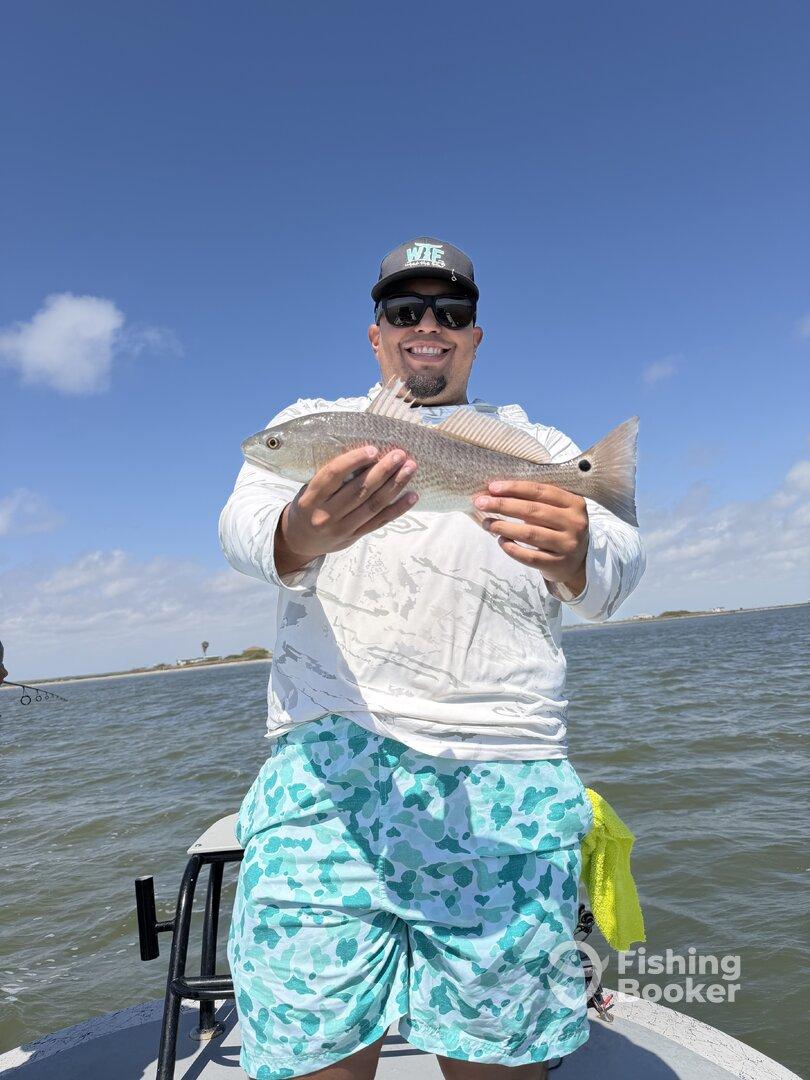 Angler proudly displaying a Redfish while fishing on a sunny day, showcasing the excitement of a successful catch.