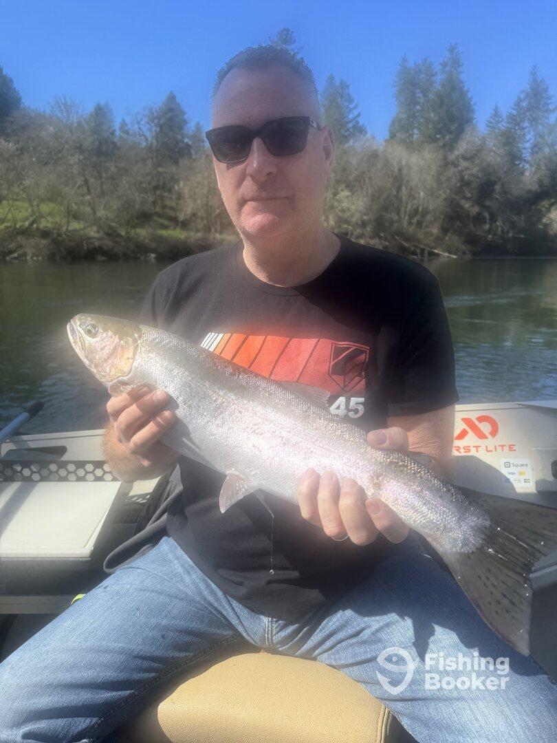 Angler proudly displaying a Rainbow Trout while fishing on a scenic river.