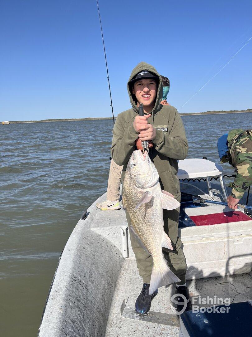 A young angler proudly displaying a large Redfish while fishing on a boat in calm waters.