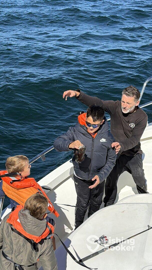 A young angler proudly displays a fish while surrounded by family on a fishing charter.