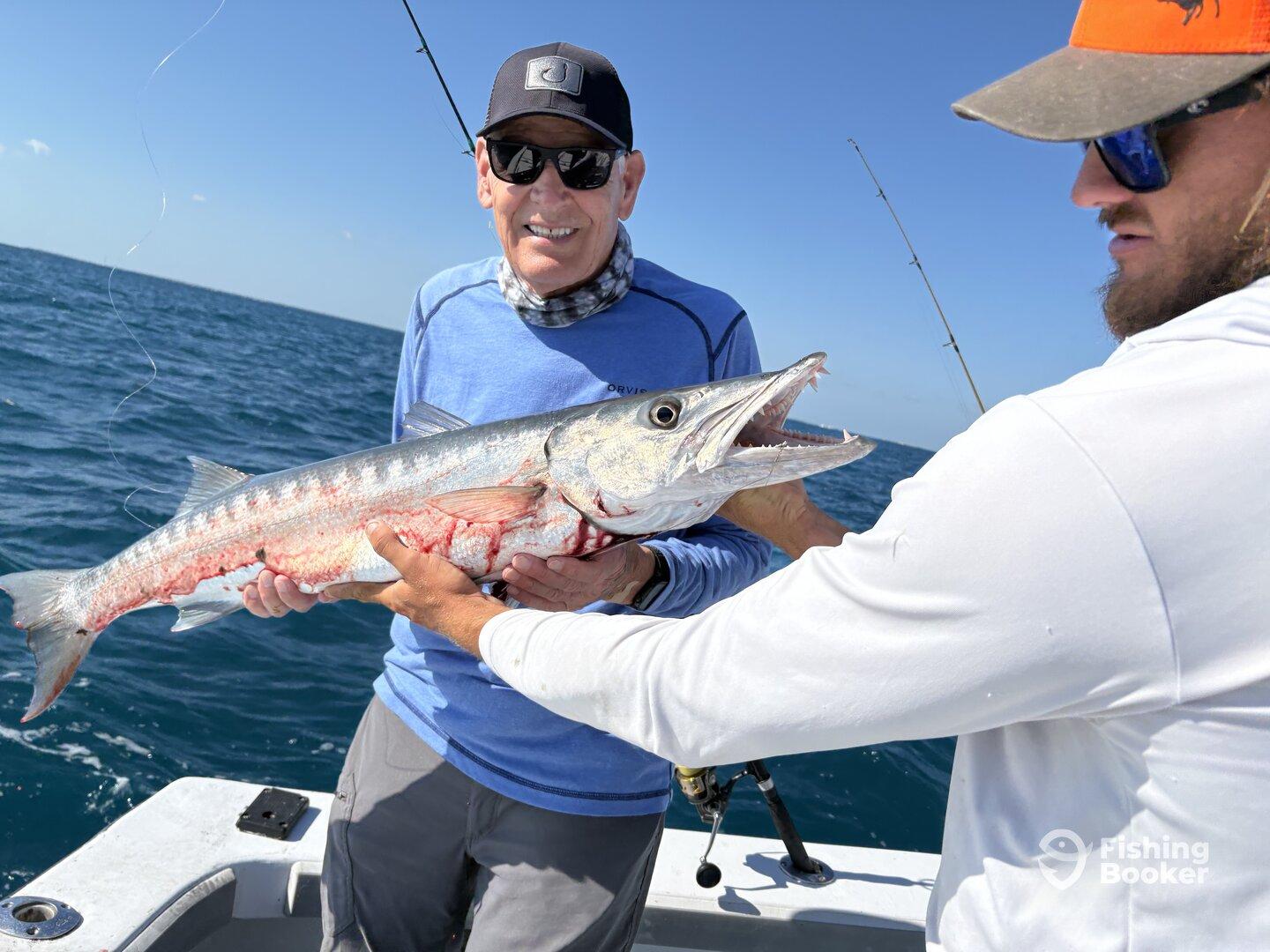 Angler proudly displaying a large Barracuda while fishing on a sunny day, showcasing a successful catch.