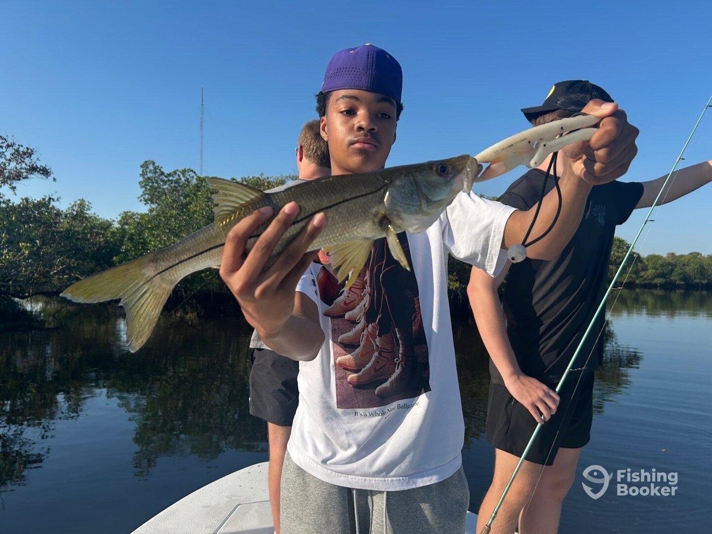 Young angler proudly displaying a Snook while fishing in a scenic mangrove area.